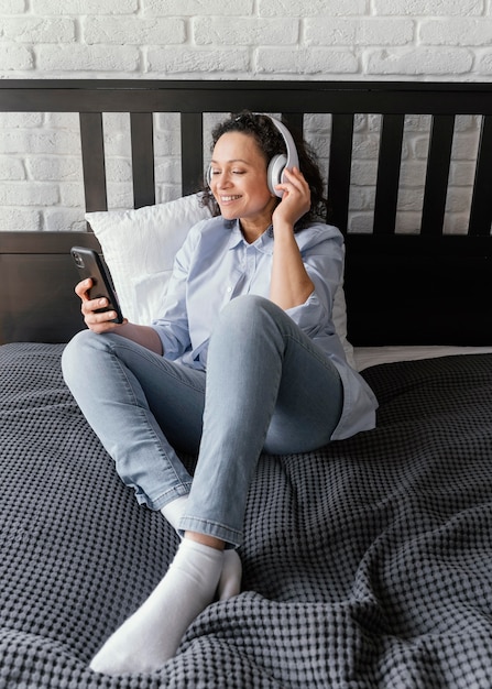 Foto mujer de tiro completo en la cama con teléfono