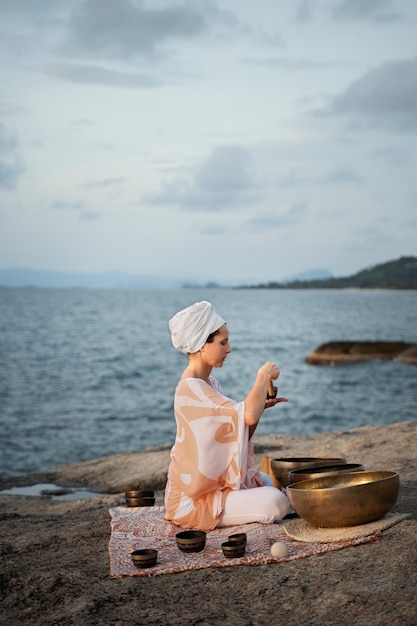 Mujer de tiro completo con cuencos curativos en la playa