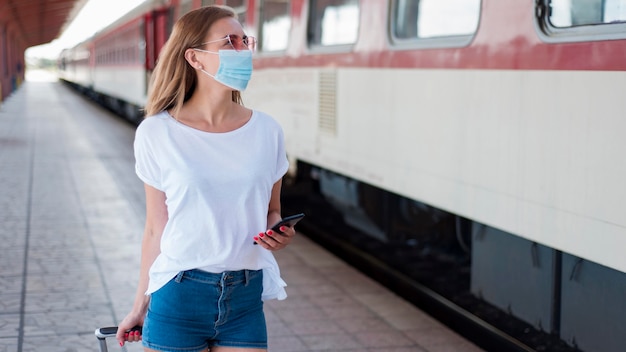 Mujer de tiro medio con máscara caminando por tren