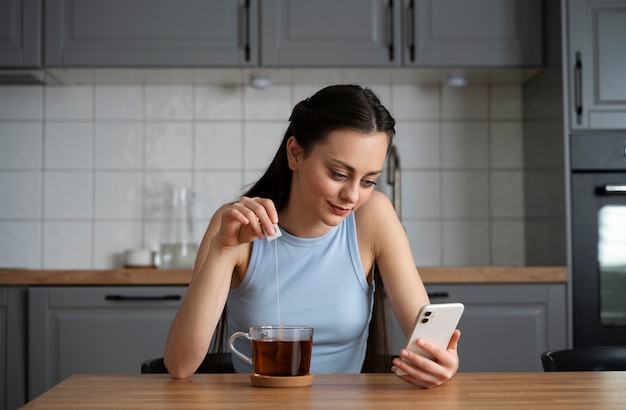 Foto mujer de tiro medio con teléfono en la cocina