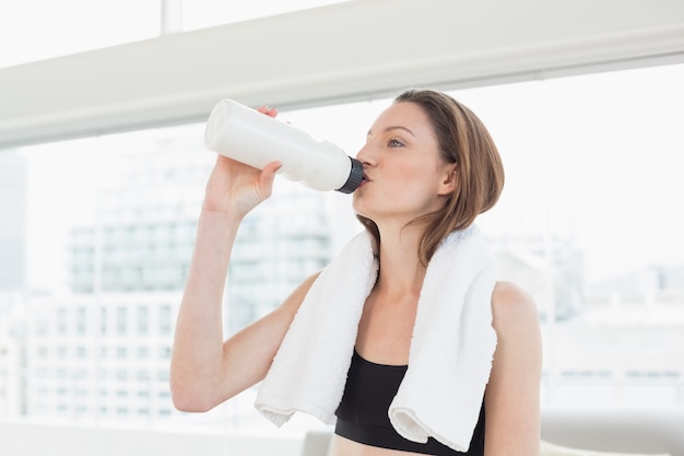 Mujer con toalla alrededor del cuello agua potable en el gimnasio