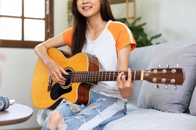 la mujer toca la guitarra y practica para cantar la canción mientras se sienta en el cómodo sofá