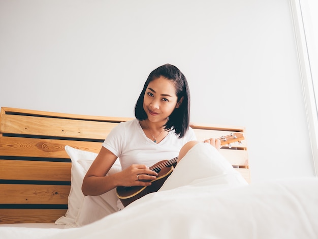 Mujer toca el ukelele en su cama por la mañana.