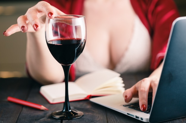 Mujer tocando una copa de vino tinto y usando su computadora portátil