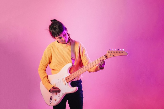 Mujer tocando la guitarra contra un fondo rosa