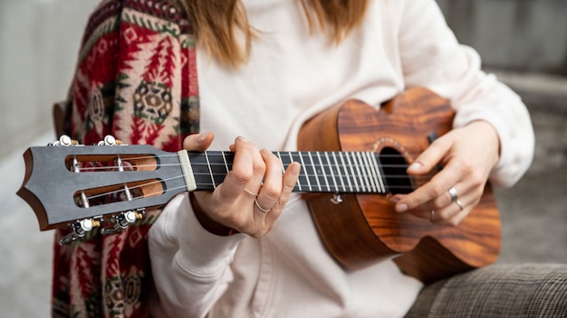 Mujer tocando la guitarra hawaiana, canta una canción en ukelele vintage en casa. Enfoque selectivo