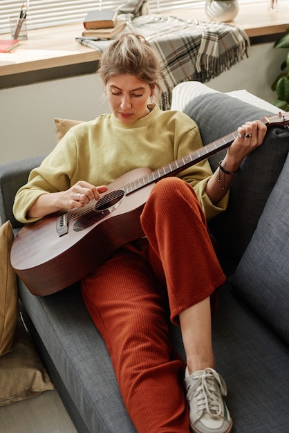 Mujer tocando la guitarra en el sofá