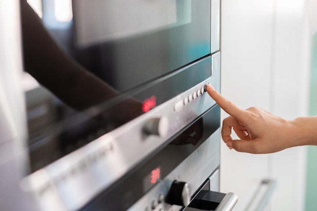 Mujer tocando el panel de control del horno eléctrico en kicthen con el dedo