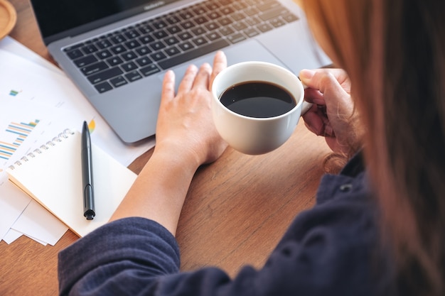 Mujer tocando en el panel táctil de la computadora portátil mientras bebe café y trabaja en la oficina