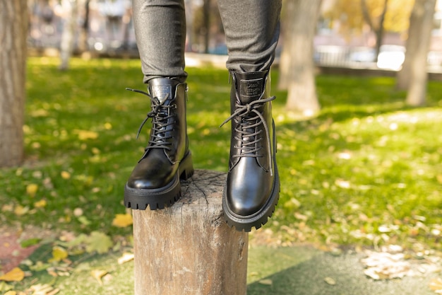 Una mujer se para en un tocón en un parque con botas negras.