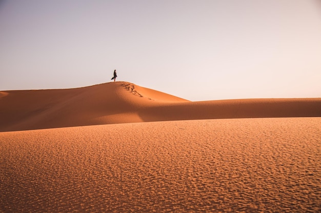 Foto mujer de toda la longitud de pie en una duna de arena en el desierto contra el cielo