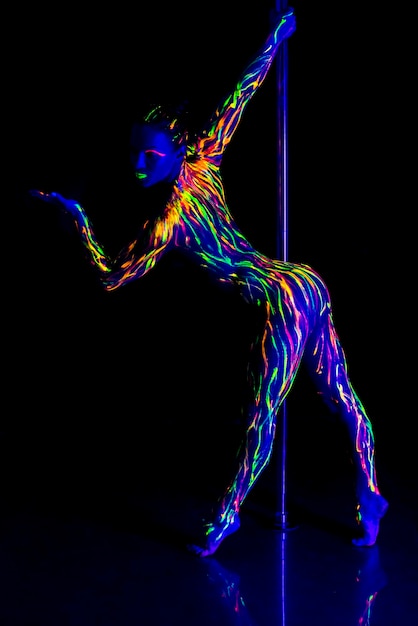 Mujer de toda la longitud con ropa de neón haciendo pole dance contra un fondo negro