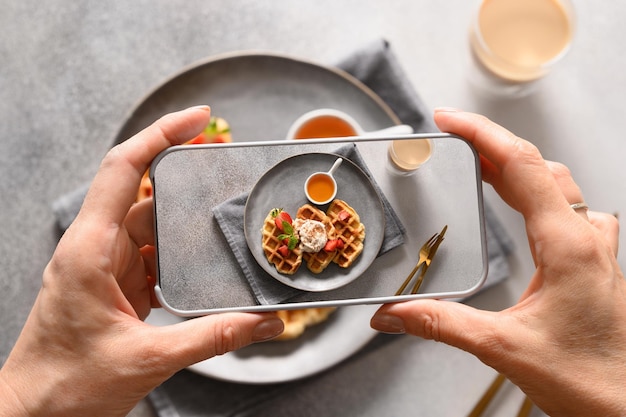 Mujer toma una foto del desayuno de croffles y café con un teléfono inteligente