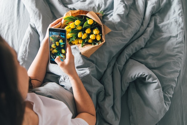 Mujer toma foto de ramo de tulipanes amarillos sorpresa romántica en la cama