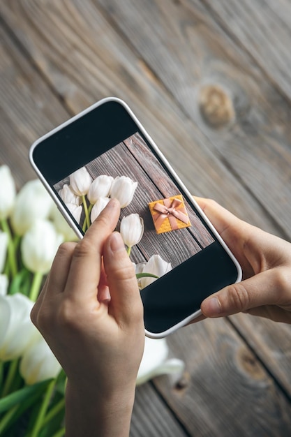 Foto mujer toma una foto de un ramo de tulipanes blancos y una caja de regalos