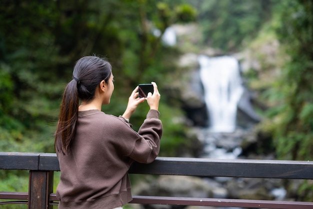 Mujer toma una foto en el teléfono móvil con una cascada