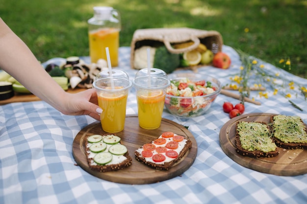 Mujer toma jugo de naranja fresco en un picnic vegano al aire libre Picnic en una manta azul a cuadros en el parque Concepto de comida vegana