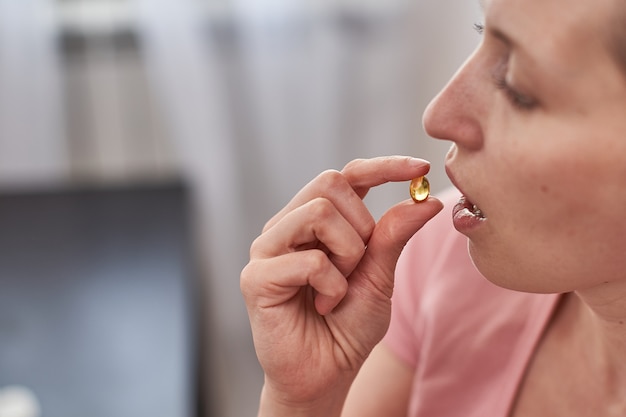 Una mujer toma una tableta con aceite de pescado en cápsulas. la niña trae la cápsula amarilla a su boca