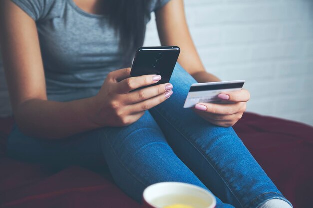 La mujer toma la tarjeta de crédito y mira el teléfono en la cama