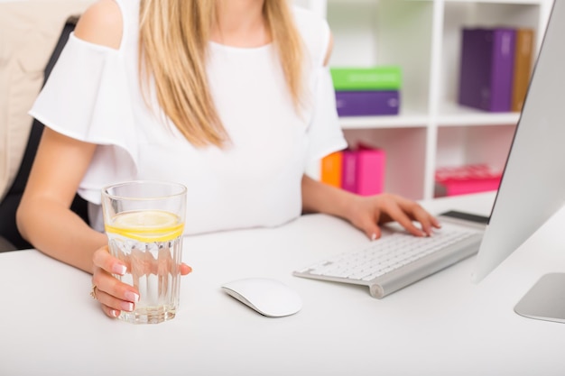 Mujer tomando agua con limón en la oficina.