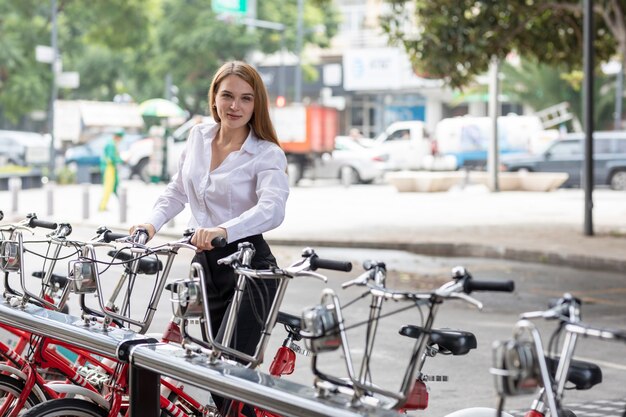 Mujer tomando una bicicleta de aplicación para moverse por la ciudad utilizando transporte sostenible