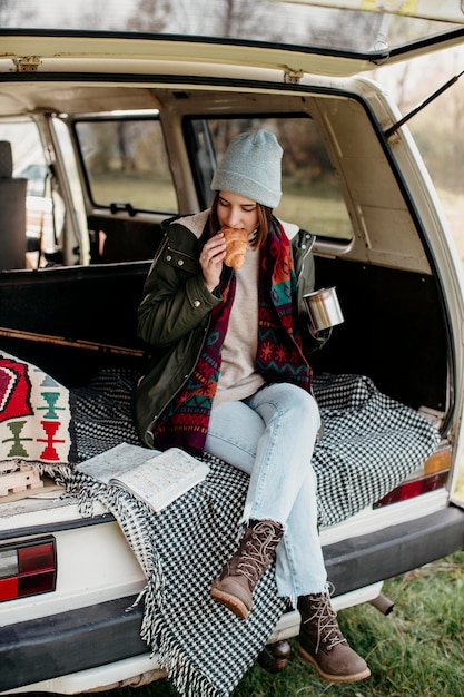 Foto mujer tomando café y comiendo un croissant en una furgoneta