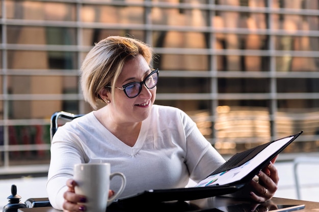 Mujer tomando café y consultando documentos de trabajo.