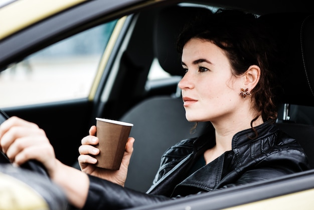 Mujer tomando un café mientras conduce un automóvil.