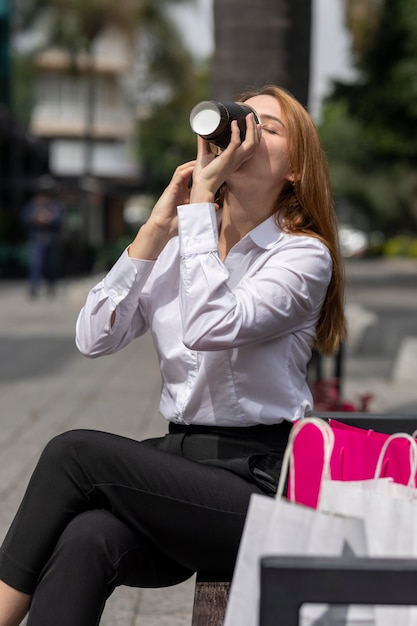 Mujer tomando café mientras descansa después de ir de compras en la zona comercial