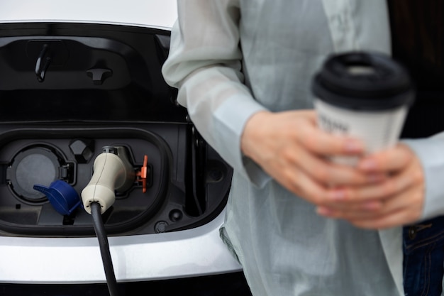 Mujer tomando un descanso para tomar café mientras su auto eléctrico se está cargando