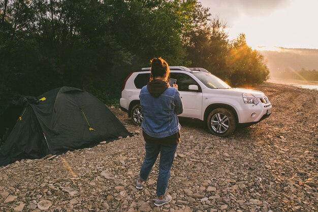 Mujer tomando una foto del amanecer en su auto teléfono acampando