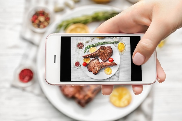 Mujer tomando una foto de deliciosos filetes grillados en la mesa de la cocina
