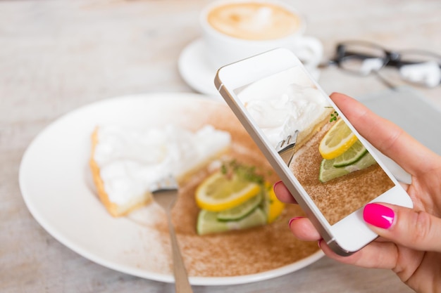 Mujer tomando una foto de su pastel en un café con teléfono móvil