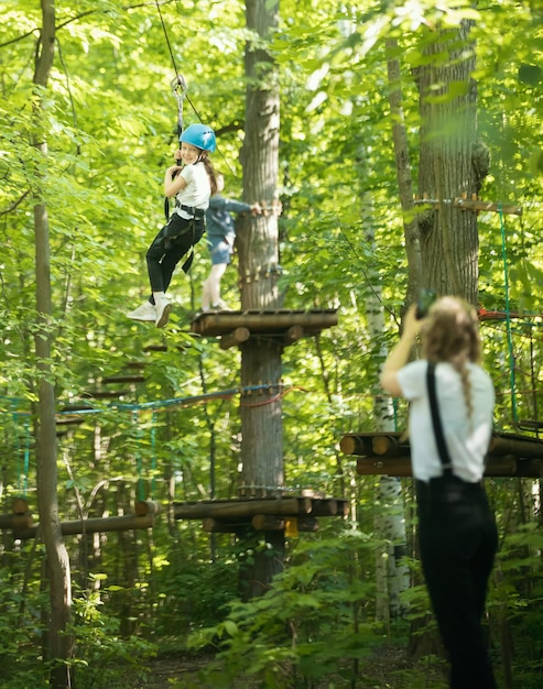 Una mujer tomando una foto de su pequeña hija colgada en el cinturón de seguros en el bosque y entretenimiento en el parque de atracciones