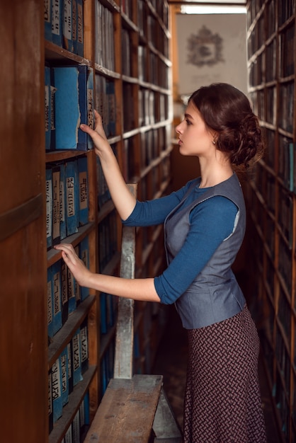 Foto mujer tomando un libro de la estantería.