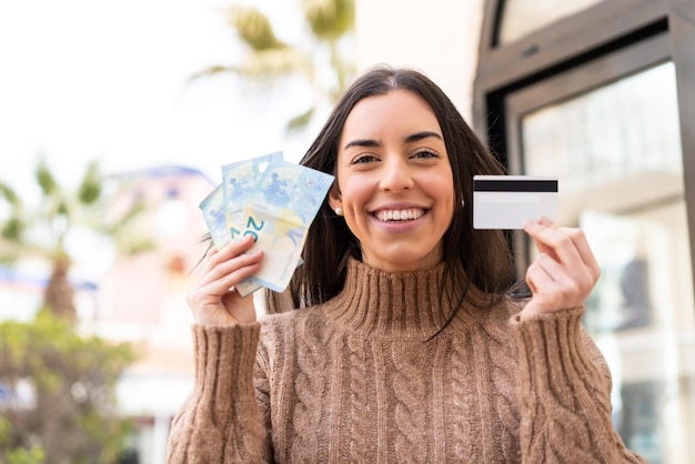 Mujer tomando mucho dinero y una tarjeta de crédito al aire libre