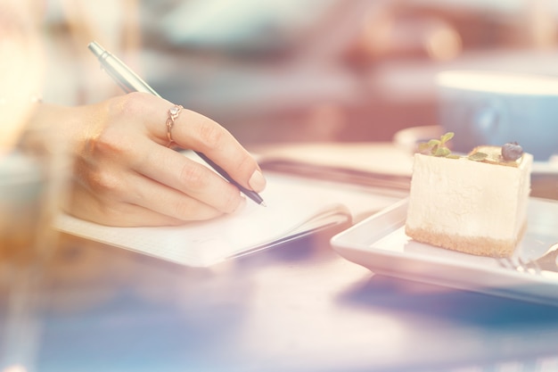 Mujer tomando notas mientras está sentado en una cafetería.