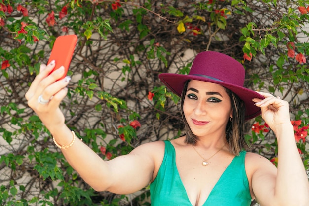 Mujer tomando un selfie en la calle. Lleva un sombrero rojo y un vestido verde.