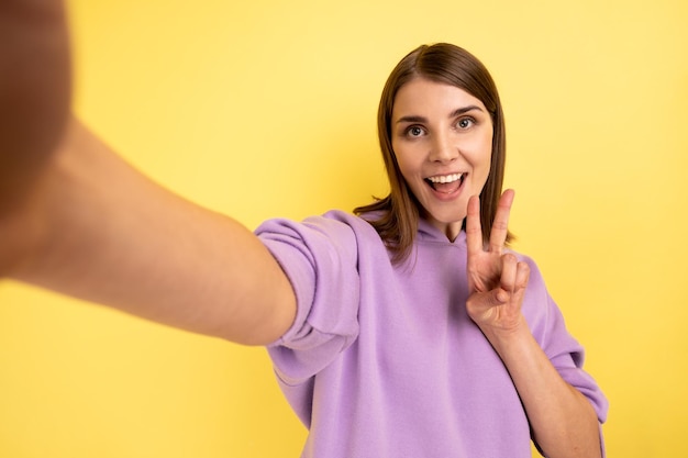 Mujer tomando selfie mirando el punto de vista de la cámara POV de la foto que muestra el gesto de la victoria