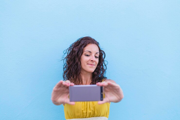 Foto mujer tomando una selfie en su teléfono móvil contra un cielo azul claro
