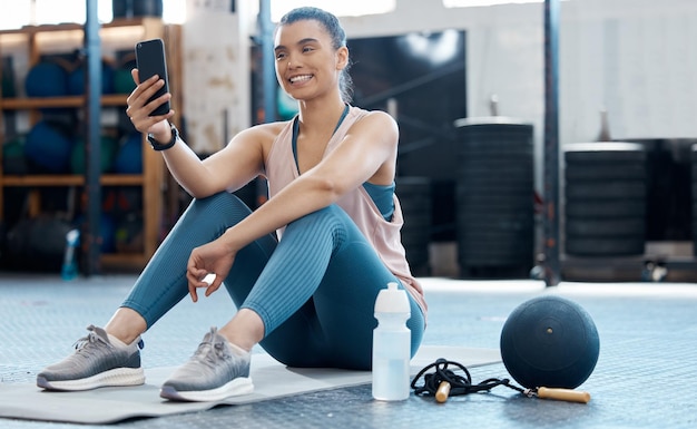 Mujer tomando selfie con el teléfono después de hacer ejercicio en el gimnasio leyendo una publicación en las redes sociales y relajándose después del ejercicio cardiovascular en el club Chica atleta en la aplicación móvil para deportes mientras entrena en el piso