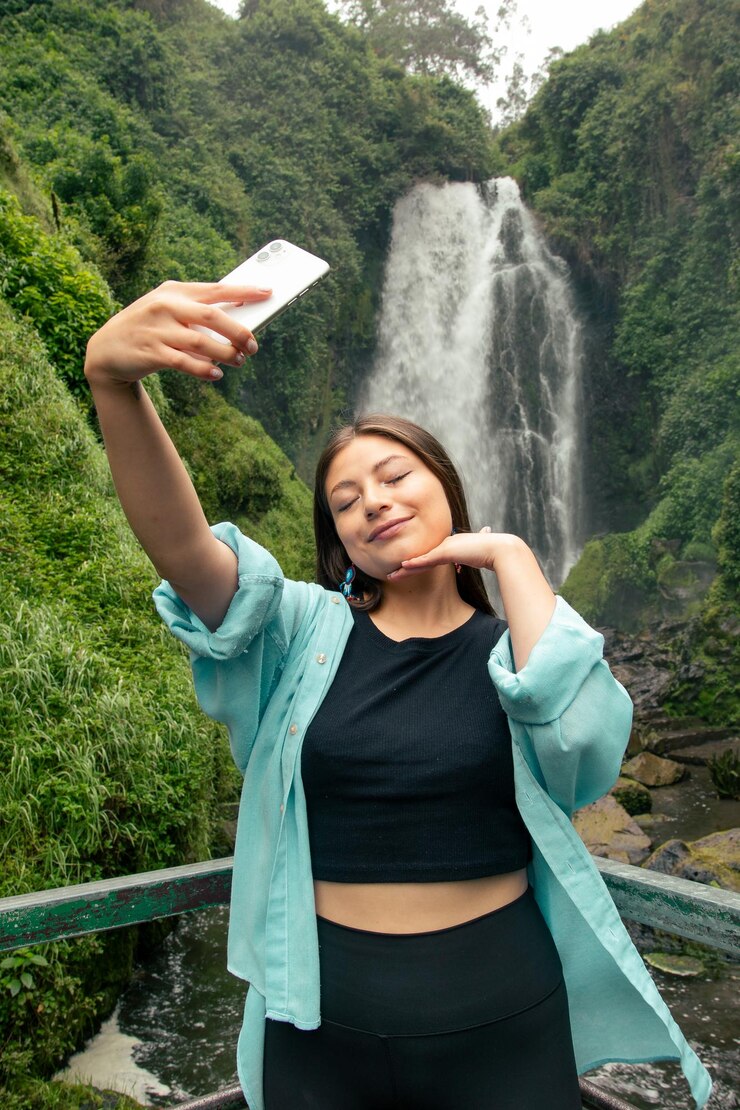 Foto una mujer tomando una selfie con un teléfono frente a una cascada