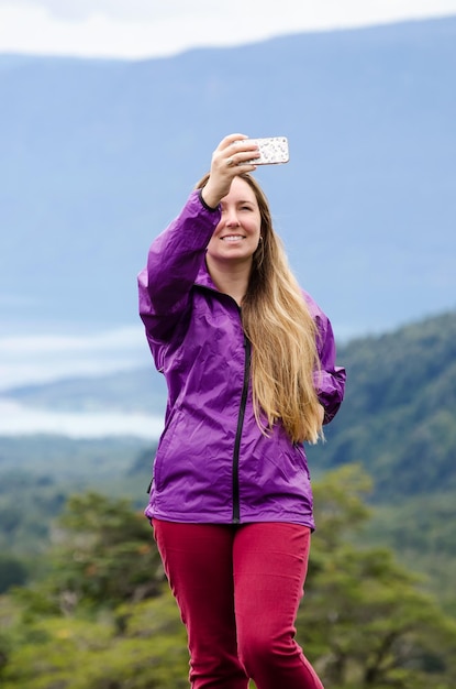 Foto mujer tomando selfies a través del teléfono móvil mientras está de pie contra las montañas