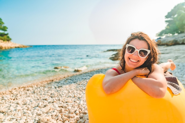 Mujer tomando el sol en la playa del mar recostada en un sofá de aire amarillo