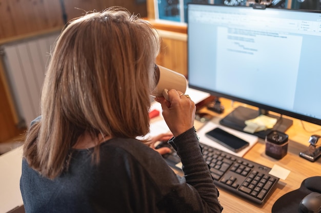Mujer tomando una taza de café mientras trabaja remotamente desde casa