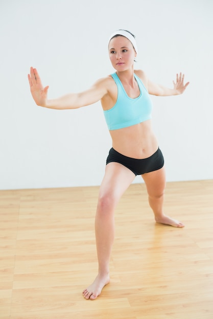 Mujer tonificada haciendo la pose de yoga Guerrero en gimnasio