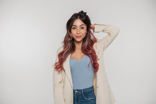 Una mujer con un top azul y jeans se para frente a un fondo blanco.