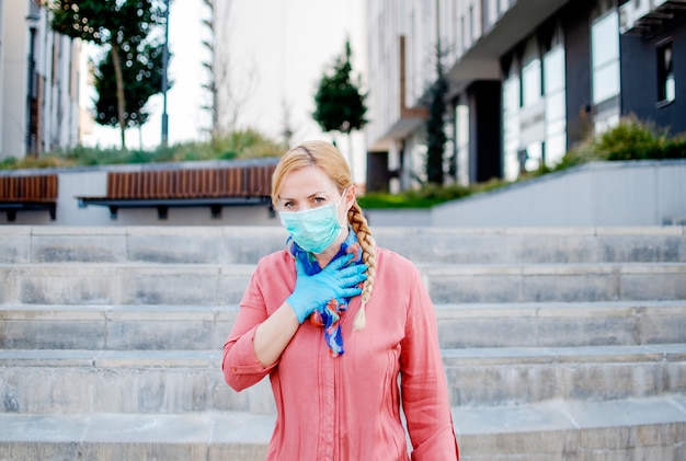 Foto mujer tosiendo con máscara médica protectora en la calle, con el síntoma covid-19. mujer joven con ropa protectora de seguridad en la ciudad durante el coronavirus