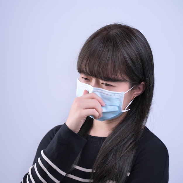 Mujer tosiendo con mascarilla joven asiática cubriendo la boca sintiéndose mal con el uso de mascarilla azul médica aislada en fondo blanco de cerca