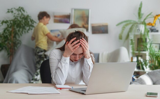 una mujer trabaja en casa con una computadora portátil, los niños interfieren con el trabajo remoto.